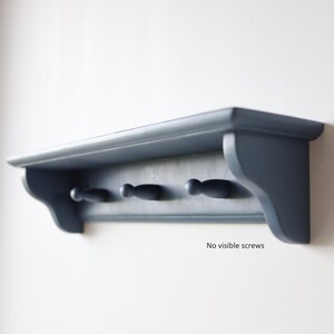 May include: A navy blue wall shelf with three pegs. The shelf has a curved front edge and decorative side supports. The text "No visible screws" is printed on the shelf.