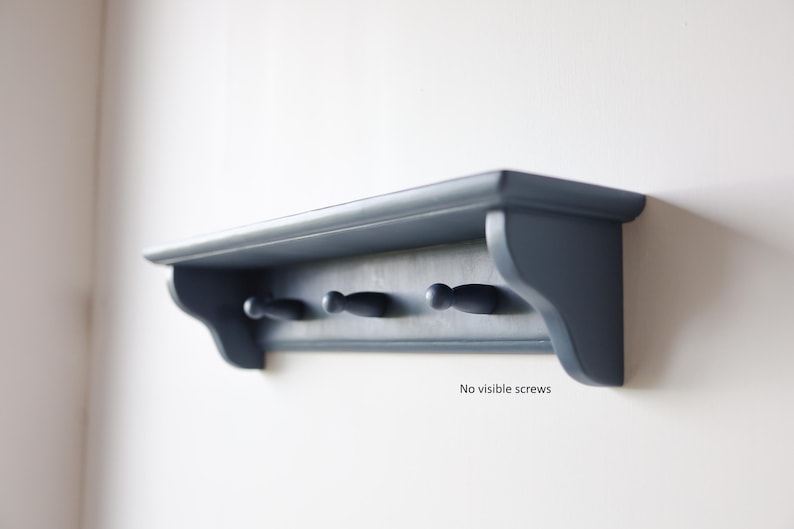 May include: A navy blue wall shelf with three pegs. The shelf has a curved front edge and decorative side supports. The text "No visible screws" is printed on the shelf.