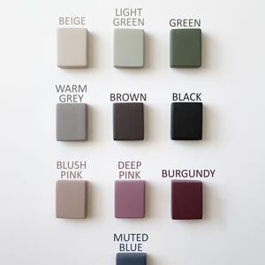 May include: A collection of twelve square-shaped objects in various colors, including beige, light green, green, warm grey, brown, black, blush pink, deep pink, burgundy, and muted blue. Each object has a color name printed above it.