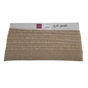 May include: A sample of beige fabric ribbon with a textured, woven appearance. The ribbon is displayed on a white card with the text "3.6 yards". The fabric is likely used for crafting or decorative purposes.