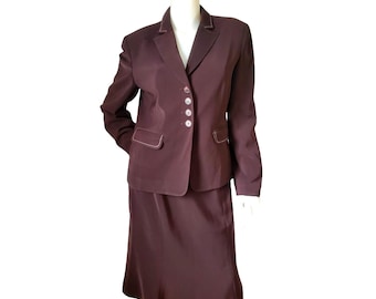May include: A dark brown skirt suit displayed on a mannequin. The suit includes a blazer with three buttons and a skirt. The blazer has white stitching around the lapels and pockets. The skirt is knee-length.