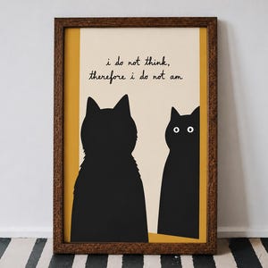 May include: A framed wall art print featuring two black cat silhouettes against a cream and mustard yellow background. The text reads, i do not think, therefore i do not am, in a simple black script. The frame is a textured dark brown wood.