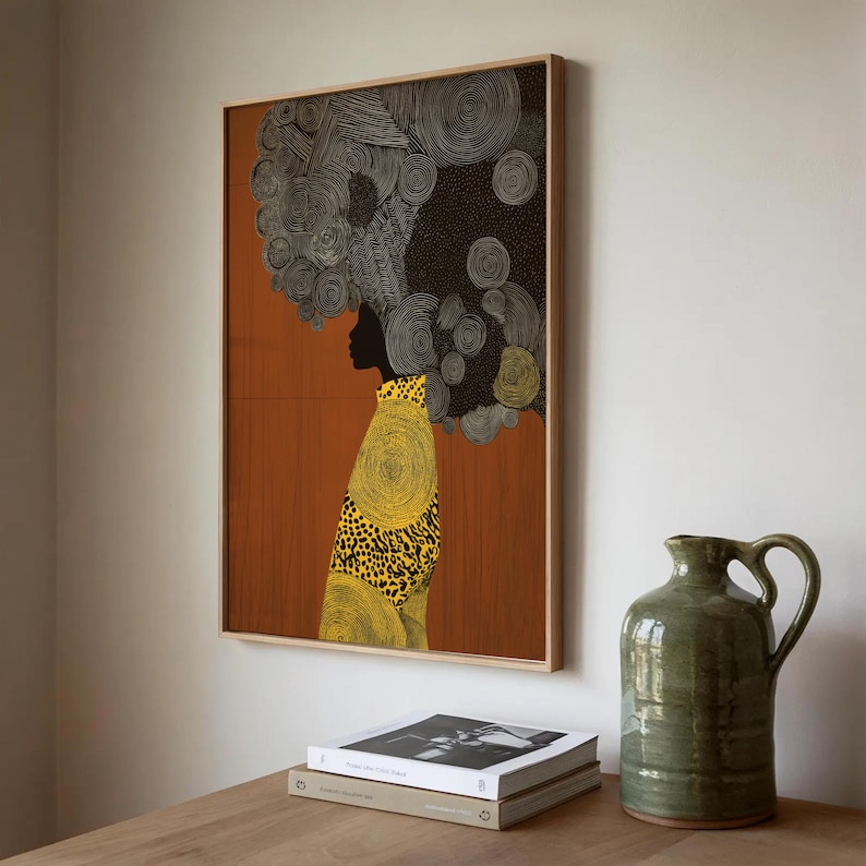 Pu&ograve; includere: Stampa artistica incorniciata raffigurante una silhouette con un'acconciatura strutturata. L'opera d'arte presenta una calda tavolozza di colori con un capo a fantasia giallo e nero. Un boccale di ceramica verde e libri sono su una superficie di legno.