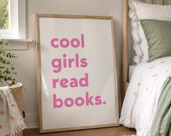 May include: A rectangular framed wall art piece featuring a white background with the text "cool girls read books." printed in bold, bright pink sans-serif letters. The artwork is encased in a light-toned wooden frame with a clean finish.