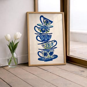 May include: A framed print featuring a stack of blue teacups with floral designs. The teacups are in a vertical arrangement, with each cup and saucer displaying a unique pattern. The artwork is set against a cream background, with a wooden frame.