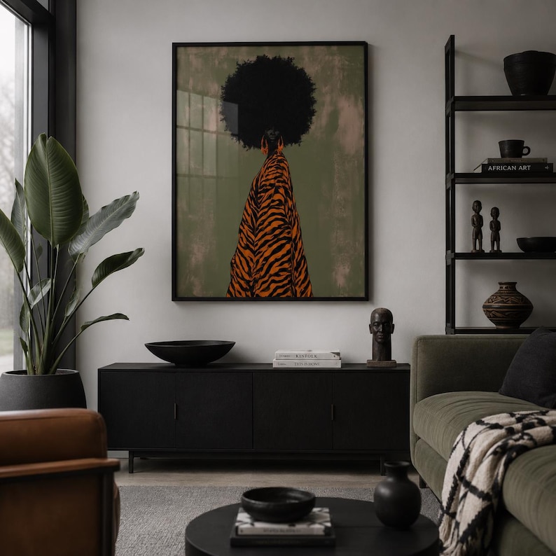 May include: A framed wall art print featuring a person with a large afro hairstyle seen from behind, wearing a long orange and black tiger-striped garment against a muted olive green background. The artwork is displayed in a black frame.