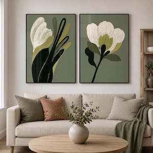 May include: Two rectangular wall art prints featuring stylised botanical illustrations on a sage green background. The left print displays an elongated white flower with dark green leaves, while the right print shows a large white blossom with olive accents.