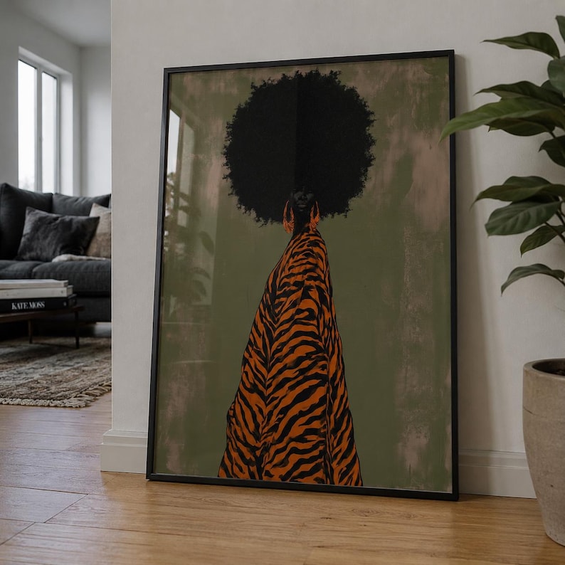 May include: A framed wall art print featuring a stylized illustration of a person with a large afro hairstyle wearing a flowing orange and black tiger-striped garment and large orange hoop earrings against a muted olive green background.