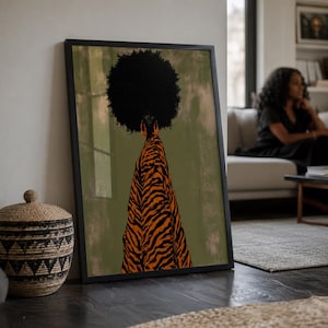 May include: A framed wall art print featuring a stylized illustration of a person with a large afro hairstyle wearing a flowing orange and black tiger-striped garment against a muted olive green background with a subtle textured effect.