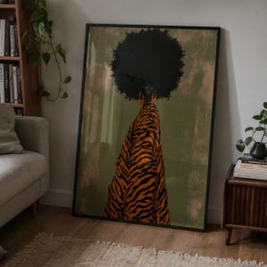 May include: A framed wall art print featuring a stylized illustration of a person with a large black afro hairstyle, wearing a flowing orange and black tiger-striped garment against a muted olive green background with textured brushstroke details.