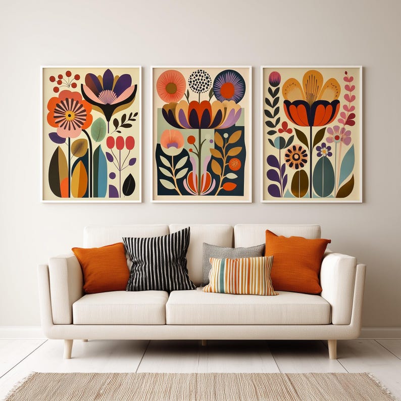 Framed colorful folk floral wall art print hanging above a wood table in a minimal neutral room, styled with stacked books and a green ceramic pitcher.