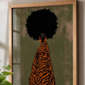 May include: A framed wall art print featuring a person with a large black afro hairstyle wearing a tiger-striped orange and black garment and large orange hoop earrings. The background is a solid muted olive green color within a light wood frame.