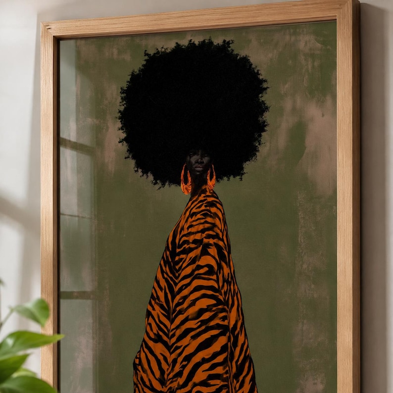 May include: A framed wall art print featuring a person with a large black afro hairstyle wearing a tiger-striped orange and black garment and large orange hoop earrings. The background is a solid muted olive green color within a light wood frame.