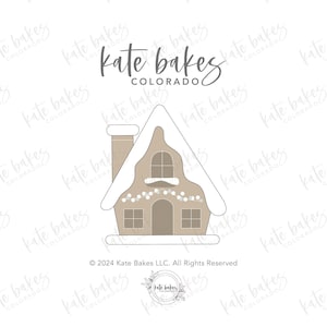 May include: A gingerbread house cookie cutter with a white roof and a chimney. The cutter is decorated with white icing and a string of lights. The text "Kate Bakes Colorado" is at the top of the image.