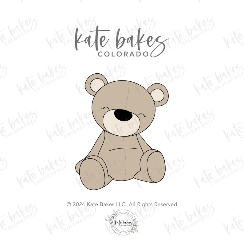 May include: A light brown teddy bear sitting with its legs crossed. The bear has a small black nose and a stitched smile. The text "Kate Bakes Colorado" is written above the bear.