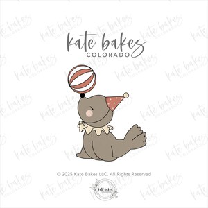 May include: A cartoon illustration of a seal balancing a striped ball on its nose. The seal is wearing a party hat and a ruffled collar. The text "Kate Bakes Colorado" is at the top.