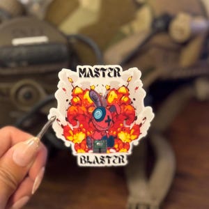 Könnte beinhalten: Ein Aufkleber mit einem Cartoon-Kaninchen mit Knopfauge, umgeben von einer Explosion aus roten und orangen Flammen. Der Aufkleber trägt die Worte "MASTER" und "BLASTER" in weißer Schrift.