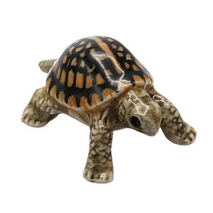 May include: A small ceramic turtle figurine with a brown, black, and orange shell. The turtle is walking forward with its head down.