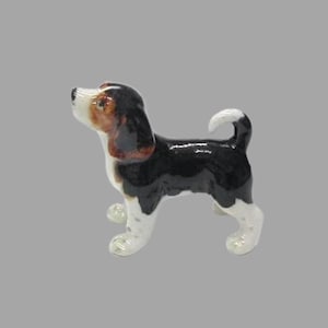 Può includere: Una piccola statuetta in ceramica di un beagle bianco e nero con macchie marroni sulla testa. Il cane è in piedi su tutte e quattro le zampe con la testa inclinata verso l'alto.