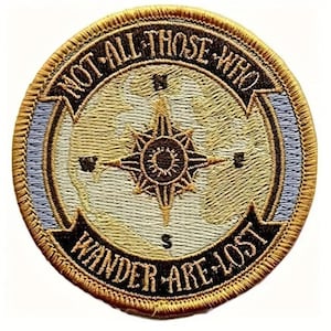 May include: Round embroidered patch with a compass design and the text "NOT ALL THOSE WHO WANDER ARE LOST." The patch features a gold border, a tan background with a map design, and a dark brown compass rose.