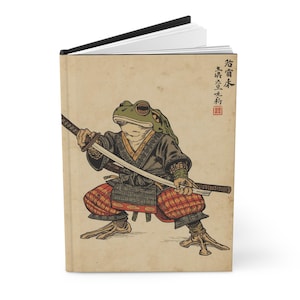 Peut inclure: Journal à couverture rigide avec une illustration de grenouille samouraï. La grenouille est vêtue d'habits japonais traditionnels, tenant deux épées. Le journal a une tranche noire et des pages vierges. Le fond est de couleur parchemin vintage.