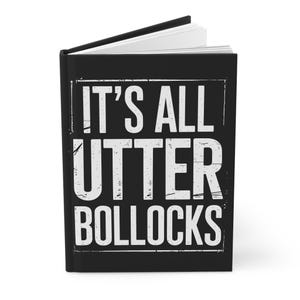May include: Black journal with the text "IT'S ALL UTTER BOLLOCKS" in white, distressed font. The journal is open, revealing white pages. The cover has a rectangular border around the text.