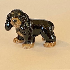 May include: A ceramic figurine of a Cavalier King Charles Spaniel dog. The dog is depicted in a standing pose with a glossy black coat, tan markings on its face and paws, and long, floppy ears. The figurine has a detailed, realistic design.