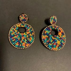 May include: A pair of colorful beaded earrings with a gold-toned metal backing. The earrings are round and have a circular cutout in the center. The beads are arranged in a circular pattern and are in shades of blue, green, orange, yellow, and red.