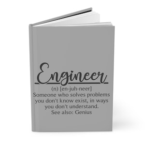 May include: A gray notebook with the word "Engineer" written in black cursive script. The definition of the word is written below in black text: "(n) [en-juh-neer] Someone who solves problems you don't know exist, in ways you don't understand. See also: Genius."