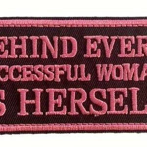 以下が含まれることがあります： 黒い背景に「Behind every successful woman is herself」というテキストが書かれたピンクの刺繍パッチ