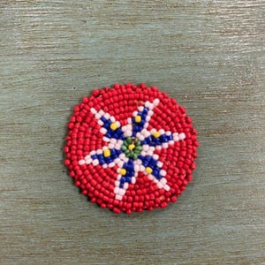 Könnte beinhalten: Ein roter Perlenkreis mit einem weißen, blauen und gelben Sternmuster in der Mitte.