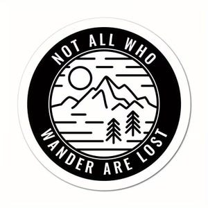 Può includere: Adesivo rotondo bianco con bordo nero. Il design presenta una catena montuosa, alberi e un sole. Il testo "NOT ALL WHO WANDER ARE LOST" è disposto a cerchio. Ideale per gli amanti dell'outdoor.