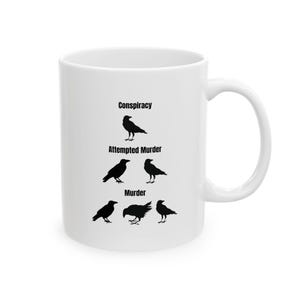 May include: White ceramic mug with a black silhouette of crows and the words "Conspiracy", "Attempted Murder", and "Murder" printed on it.