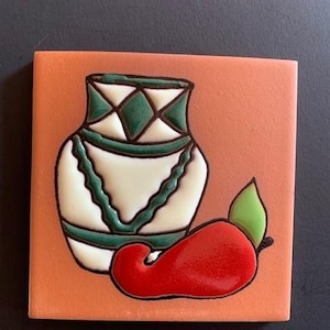 May include: A ceramic tile with a hand-painted design of a green and white patterned vase and a red chili pepper on an orange background.