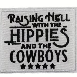 Peut inclure: Patch brodé blanc avec du texte noir qui dit "Raising Hell With The Hippies And The Cowboys" avec cinq étoiles noires en dessous du texte.