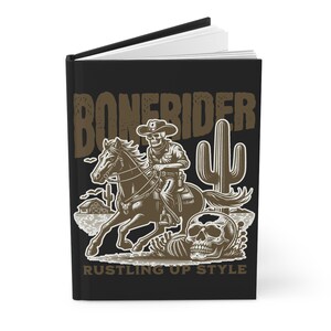 May include: Black journal featuring a brown illustration of a skeleton cowboy riding a horse, with a cactus and skull. The text "BONERIDER" and "RUSTLING UP STYLE" are also featured on the cover.