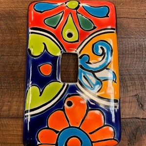 Pode incluir: Uma tampa de interruptor de luz de cerâmica colorida com um design floral em tons de azul, verde, laranja, amarelo e vermelho.