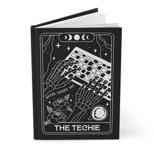 Pode incluir: Diário preto com uma ilustração branca de mãos de esqueleto digitando em um teclado. O design inclui o texto "NEVER LOGGED OFF" e "THE TECHIE". A capa também apresenta rosas, estrelas e luas crescentes.
