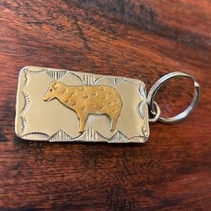 May include: Silver and gold key chain with a detailed design of a sheep. The sheep is gold with a silver outline.