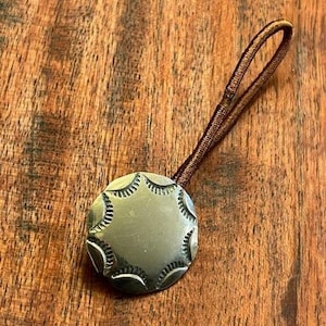 Puede incluir: Un botón de metal plateado con un diseño de estrella, unido a un cordón marrón.