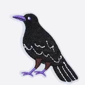 May include: Embroidered patch featuring a black crow with purple beak, feet, and eye. The crow has white stitching details on its wings and body. The patch is on a white background.