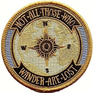 Puede incluir: Un parche redondo bordado en oro con un diseño de brújula y mapa del mundo. El texto "Not all those who wander are lost" está escrito alrededor del borde del parche.