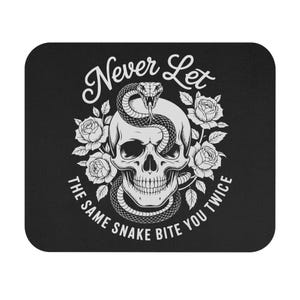 May include: Black mousepad featuring a skull with a snake coiled around it, surrounded by roses. The text reads "Never Let The Same Snake Bite You Twice" in a stylized font. The design is in white.