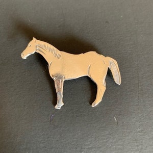 May include: A silver horse brooch with a detailed design. The horse is standing on all four legs with its head held high.