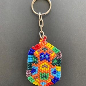 May include: A colorful beaded keychain with a geometric pattern in shades of red, orange, yellow, green, blue, and purple. The keychain is attached to a silver key ring.