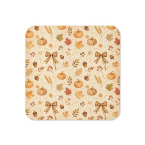 May include: A square coaster featuring a repeating pattern of orange pumpkins, brown acorns, wheat stalks, colorful autumn leaves, and plaid bows on a cream-colored background. The design elements are arranged in a balanced, decorative layout.