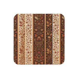 May include: A square coaster featuring a repeating vertical stripe pattern in shades of brown, cream, and orange. The design displays intricate botanical illustrations of autumn leaves, acorns, and small flowers arranged in symmetrical columns.