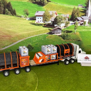 May include: A model truck and trailer set with a white cab, orange and black trailer, and several containers. The trailer has the words "Farmer Billy" on the side. The background features a green field and a small village.