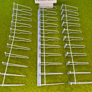 Op de afbeelding: Drie sets grijze plastic hekwerkstukken voor modeltreinen. Elke set heeft 10 hekwerkpalen en 10 rails. De sets zijn in een rij op een groene ondergrond geplaatst. De tekst "FARMER BILLY" is zichtbaar op een kaart in het midden van de afbeelding.