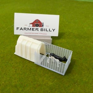 Peut inclure: Un modèle en plastique blanc d'un enclos à veau avec un modèle en plastique blanc d'un veau à l'intérieur. L'enclos est doté d'un modèle en plastique blanc d'un abri qui y est attaché. Le modèle est sur une surface d'herbe verte. Le texte "FARMER BILLY CUSTOM MADE TOYS" est sur une carte blanche derrière le modèle.